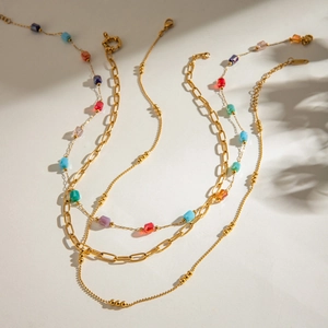 Detailed view of layered gold-tone chains with colorful square beads and soft shadows