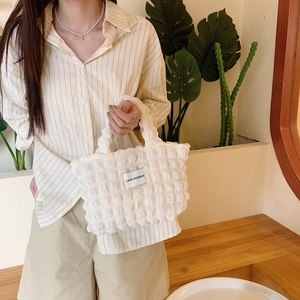 White puffy canvas handbag with texture detail and woven brand label held by a model