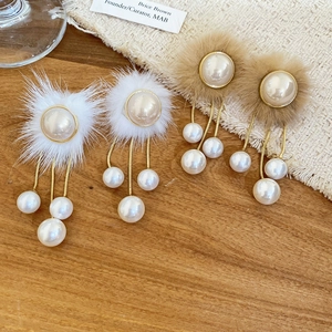 Detail of plush fur ball and pearl tassel earrings on a warm wooden surface background