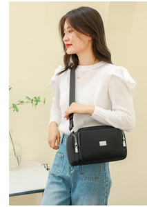 Detalle de un bolso bandolera de nailon negro con múltiples bolsillos y cremalleras de plata