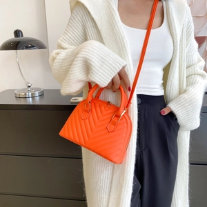 Orange quilted shell handbag with top handle and shoulder strap shown on a model