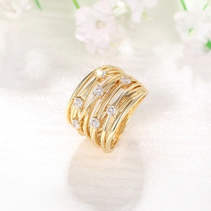 Detalle de anillo multicapa dorado con circonitas brillantes sobre un fondo floral suave
