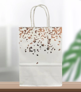 Detail of white paper gift bag with rose gold foil heart pattern and twisted handles