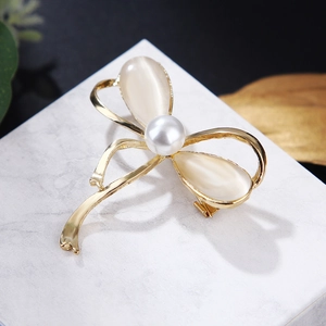 Detail of a golden bow brooch with cat eye stones and a white pearl on marble
