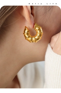 Close-up of golden croissant style earrings with ribbed texture worn by a model
