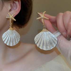 Detail of gold starfish and white shell earrings worn by a model for a beach vacation look