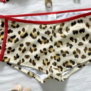Detail of leopard print bikini bottom with red trim showing material label and fabric texture