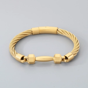Detail of gold braided steel cable bracelet featuring cylindrical clasp and geometric charms