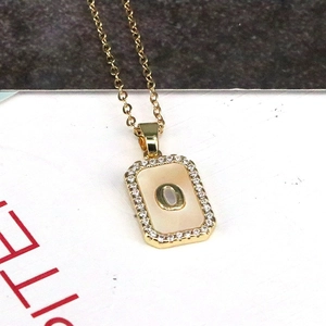Detailed macro view of 18K gold rectangle pendant with shell inlay and zircon-set letter O