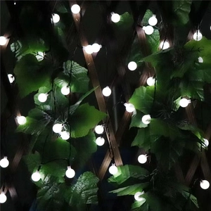 Solar powered frosted LED globe string lights with green leaves on wooden fence for garden