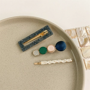 Detailed set of three hair clips featuring resin patterns and pearls on a beige plate