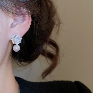 Close-up of elegant flower zircon earrings with round white pearl drop on female ear