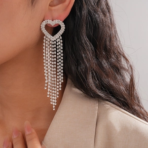 Close-up of heart-shaped dangling earrings with tassels and sparkling rhinestones on model