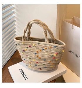 Detail of a handmade straw tote bag with colorful pom-poms and twisted rope handles