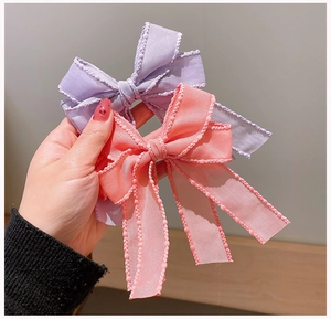 Detailed view of handmade layered bow hair clips with bead-stitched edges in purple and pink