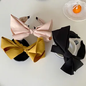 Three oversized bow headbands in pink, yellow, and black fabric on a white surface