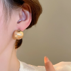 Close-up of gold dome earrings with star zircon stones and brushed matte texture