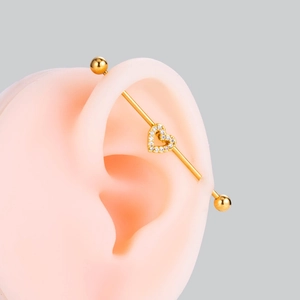 Golden industrial barbell earring with a crystal heart detail on a silicone ear model