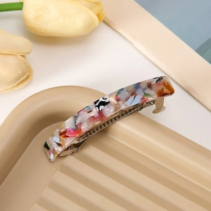 Dettaglio del fermaglio per capelli in acetato floreale su un vassoio beige
