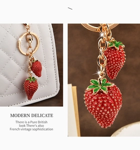 Detail of red strawberry enamel charms with gold-tone keychains on a white quilted bag