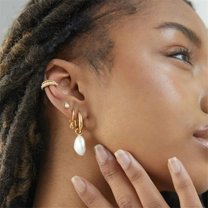 Close-up of gold hoop with pearl pendant and textured ear cuff worn on the cartilage