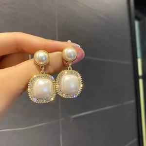 Macro detail of gold C-shaped earrings with square pearl and sparkling zircons