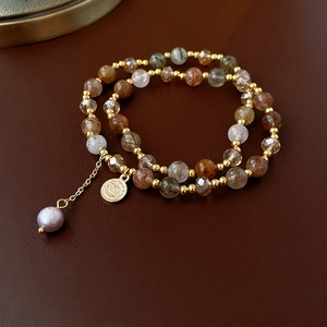 Macro shot of multi-layer rutile quartz bracelet with vintage coin and pearl charms