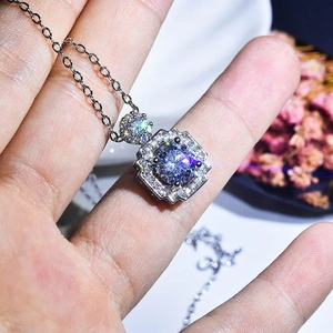 Detail of square blue stone pendant necklace held by hand against floral background