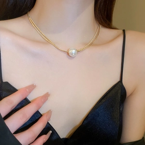 Detail of a double-layered gold snake chain necklace with a single white pearl pendant