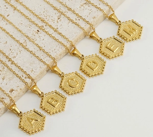 Detailed macro of golden hexagon letter pendants on fine stainless steel chain necklaces