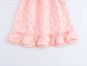 Dettaglio del tessuto jacquard rosa con trama floreale e orlo a balze su un mini abito