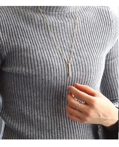 Close-up of a minimalist gold cylinder pendant necklace and silver ring on a model