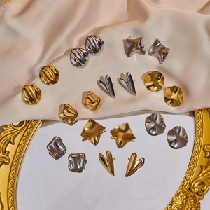 Polierte geometrische Edelstahl-Ohrringe in Gold und Silber auf beigem Satinhintergrund