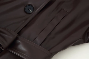 Detailaufnahme der dunkelbraunen Lederjacke mit schwarzen Knöpfen und feiner Nahtführung