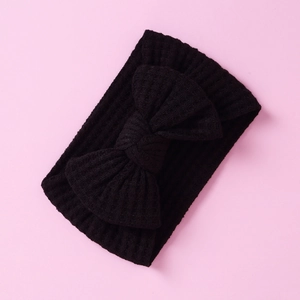 Detail of a black waffle-knit baby headband with a large bow on a pink background