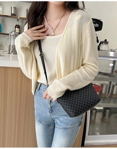Chic black textured crossbody bag styled with knit cardigan and pearl necklace in a cafe