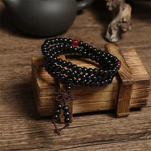 Black 108 sandalwood prayer beads with red accents and tassel on a vintage wooden box