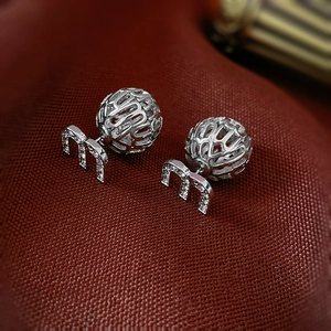 Détail de boucles d'oreilles 'm' argentées avec zircons sur un tissu en soie rouge