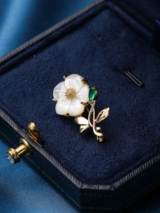Detailed close-up of shell flower brooch with green crystal in a navy velvet box