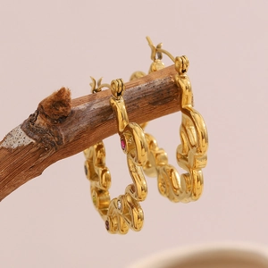 Gold hollow hoop earrings with colorful zircon stones on a rustic wooden stand