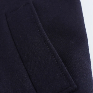 Detailed view of the dark blue herringbone wool coat showing pocket stitching and texture