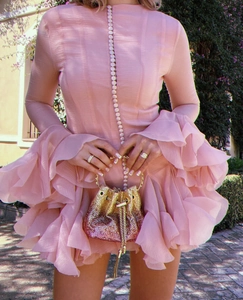 Detailed close-up of pink flared sleeve dress with ruffles and gold sequin bucket bag