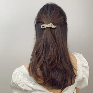 Close-up of golden bow-shaped hair clip with white pearls and sparkling rhinestones