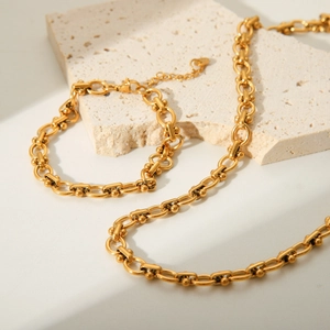Golden stainless steel U-link chain necklace and bracelet set on textured stone base