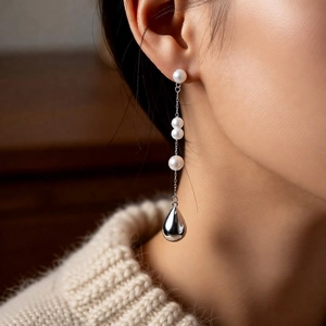Detail of silver pearl drop earring on model featuring four beads and metallic pendant