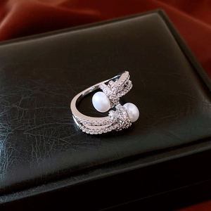 Macro shot of silver knot ring with sparkling zircon pavé and two elegant white pearls