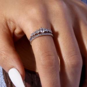 Close-up of stacked silver rings with crown diamond design on finger