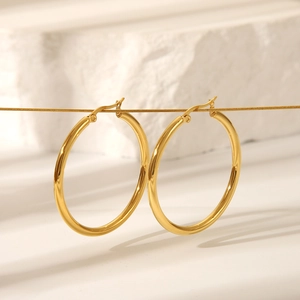 Boucles d'oreilles créoles dorées classiques en acier inoxydable sur mur texturé blanc