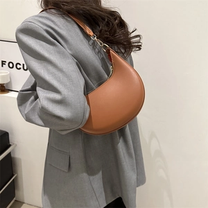 Brown faux leather crescent underarm bag with gold hardware worn by a model in a gray suit