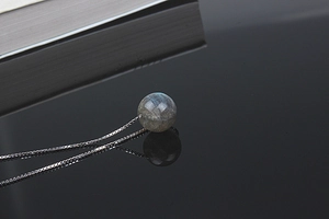Detailed view of natural labradorite pendant on silver chain over a black mirror surface